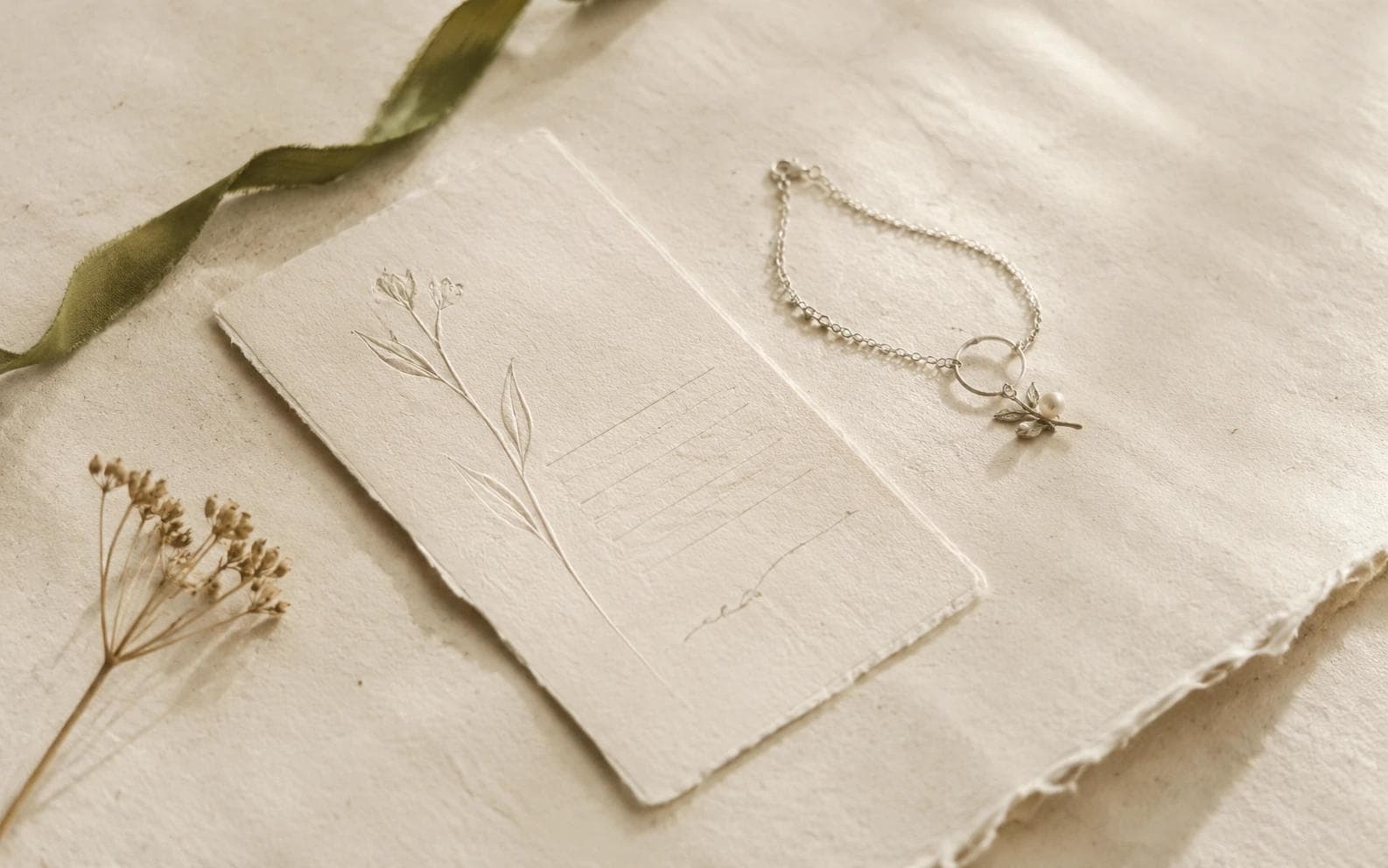 An Emotion Card in embossed handmade paper beside a silver bracelet with a pearl and leaf charm.